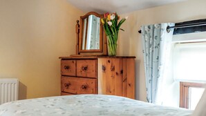 A bedroom with a wooden dresser, a mirror, and a vase with flowers. - Holly Lodge - UK36321 (Holly Hedge Farm)