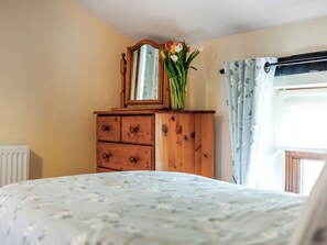 A bedroom with a wooden dresser, a mirror, and a vase with flowers. - Holly Lodge - UK36321 (Holly Hedge Farm)