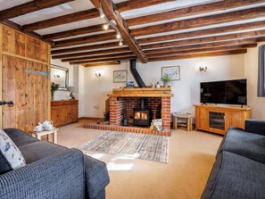 Una sala de estar acogedora con chimenea, vigas de madera, televisor y asientos cómodos.