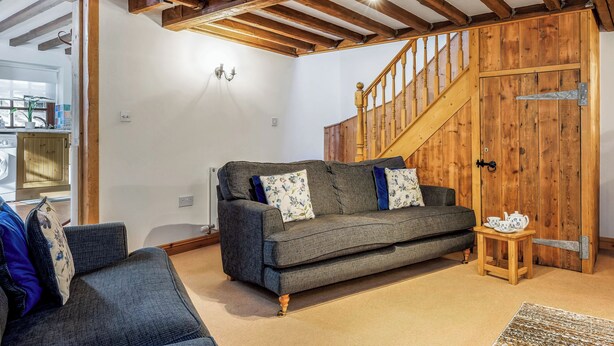 A cozy living room with a dark grey sofa, a wooden staircase, and a rustic wooden door. - Holly Lodge - UK36321 (Holly Hedge Farm)