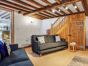 Una sala de estar acogedora con un sofá gris oscuro, una escalera de madera y una puerta de madera rústica.