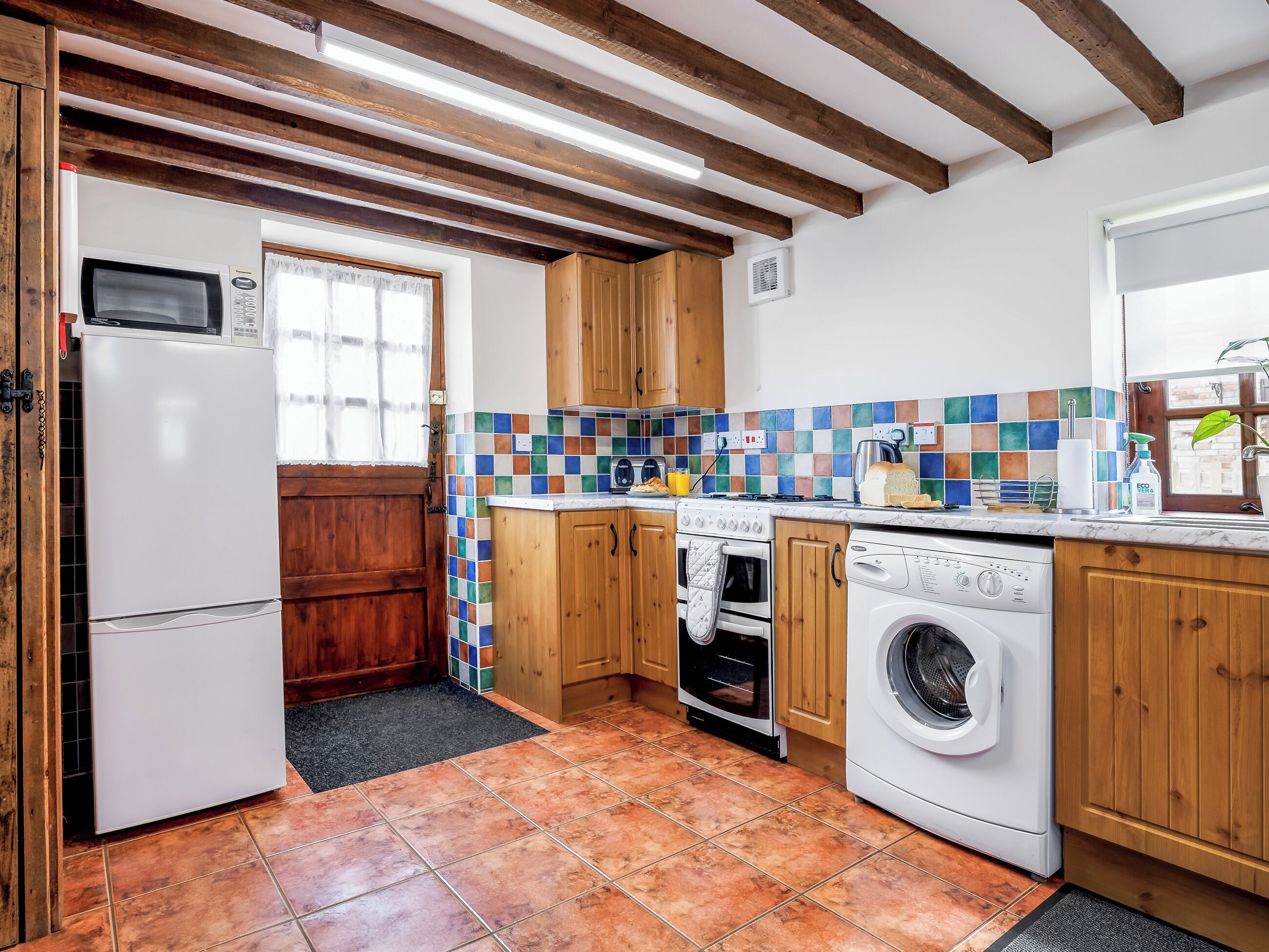 A kitchen with wooden cabinets, a microwave, an oven, a washing machine, and a tiled backsplash.