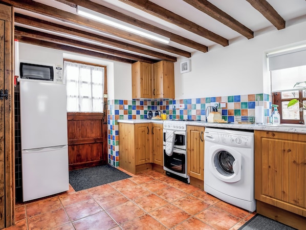 A kitchen with wooden cabinets, a microwave, an oven, a washing machine, and a tiled backsplash.
