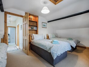 A bedroom with two beds, a wooden bookshelf, a door leading to another room, and a ceiling light fixture.