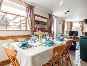 A dining area with a table set for four, wooden chairs, a vase with flowers, and a television in the background. - Robins Nest - UK36322 (Holly Hedge Farm)