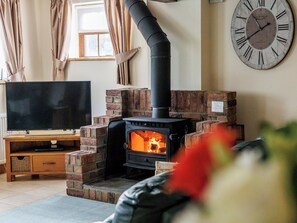 A living room with a brick fireplace, a flat-screen TV on a wooden stand, and a large wall clock.