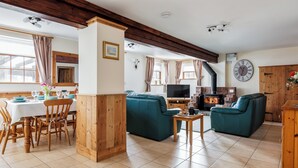 Uma sala de estar acolhedora com lareira, sofás verde-água, mesa de jantar de madeira e uma televisão.