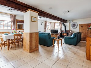 A cozy living room with a fireplace, teal sofas, wooden dining table, and a TV. - Robins Nest - UK36322 (Holly Hedge Farm)