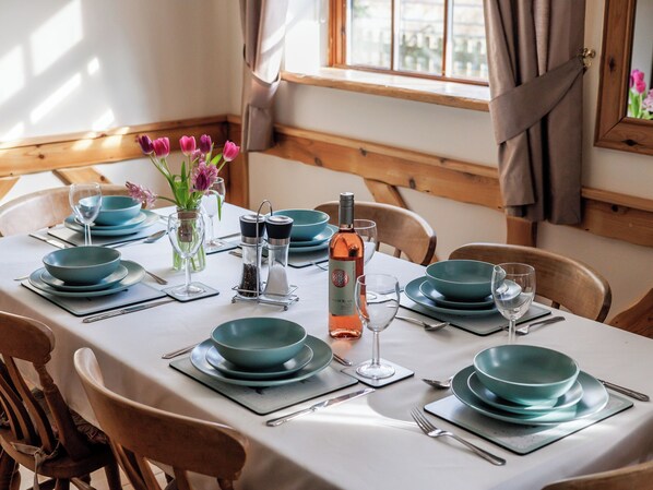 A dining table set with teal plates, glasses, and cutlery, a bottle of wine, salt and pepper shakers, and a vase with flowers. - Robins Nest - UK36322 (Holly Hedge Farm)