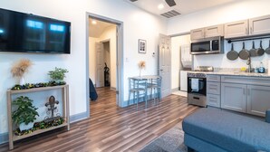 A modern kitchen with a flat-screen TV, microwave, and oven. There is a dining area with a table and chairs. - Private Uptown Cottage! Walk to Freret, Tulane & St. Charles Street Car (New Orleans)