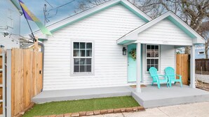 A white house with a green roof and a number 4935 on the front door. There are two turquoise Adirondack chairs outside. - Private Uptown Cottage! Walk to Freret, Tulane & St. Charles Street Car (New Orleans)