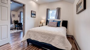 A bedroom with a large bed, a ceiling fan, a window with curtains, and a painting on the wall. - Private Uptown Cottage! Walk to Freret, Tulane & St. Charles Street Car (New Orleans)