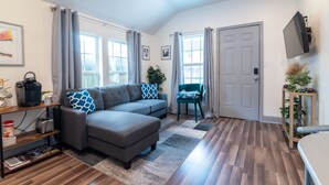 A modern living room with a sectional sofa, a coffee machine, and a TV mounted on the wall. - Private Uptown Cottage! Walk to Freret, Tulane & St. Charles Street Car (New Orleans)