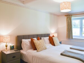 A neatly made bed with multiple pillows, a bedside table with a lamp, and a window with curtains. - 2 bedroom accommodation in Winsford (Winsford)