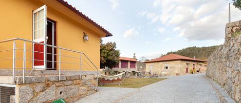 A cobblestone pathway leading to a yellow building with a red door and a stone wall on one side.