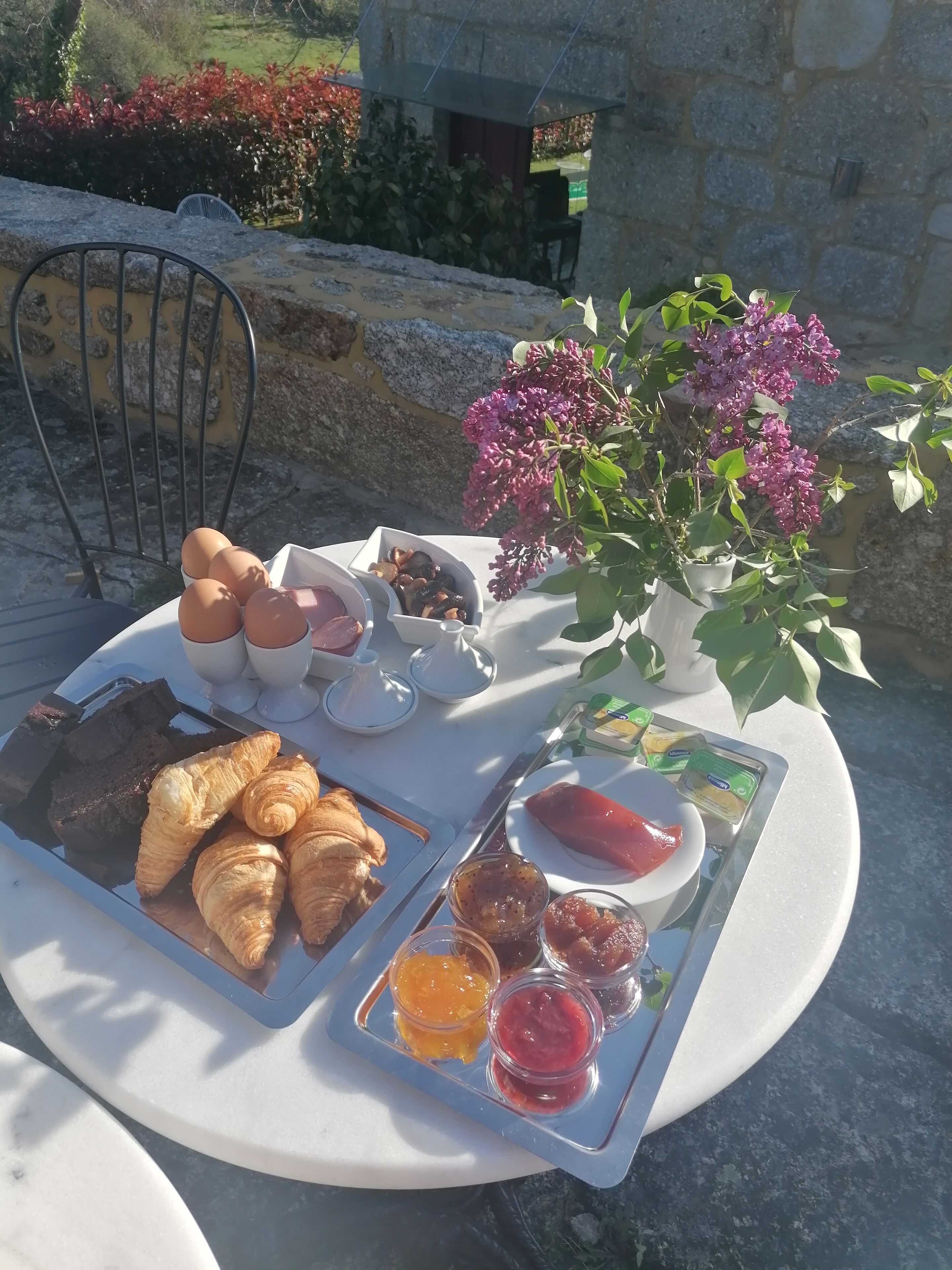 A table set with croissants, bread, jams, and a vase of flowers.