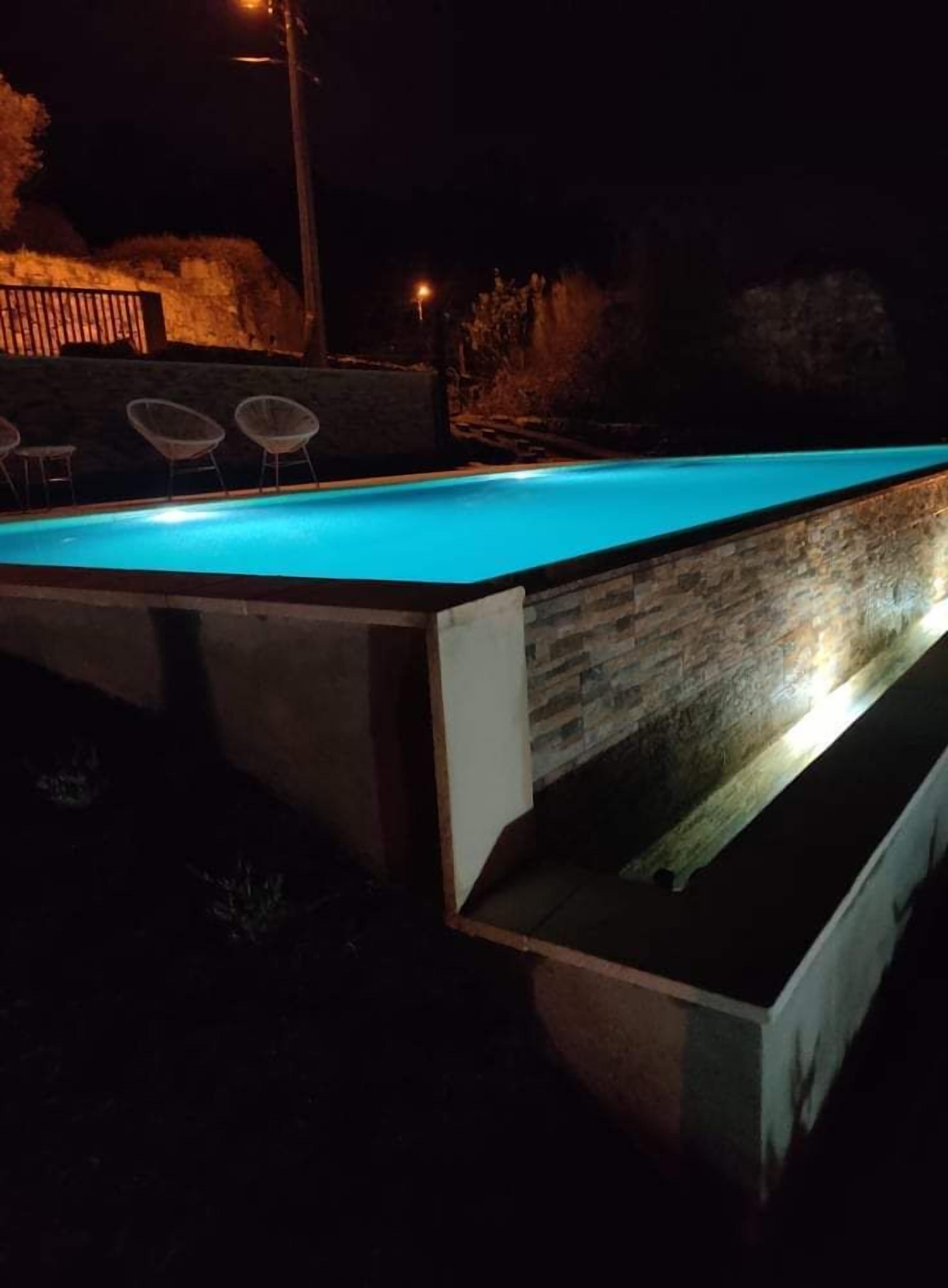 Une piscine avec un mur en pierre et quelques chaises.
