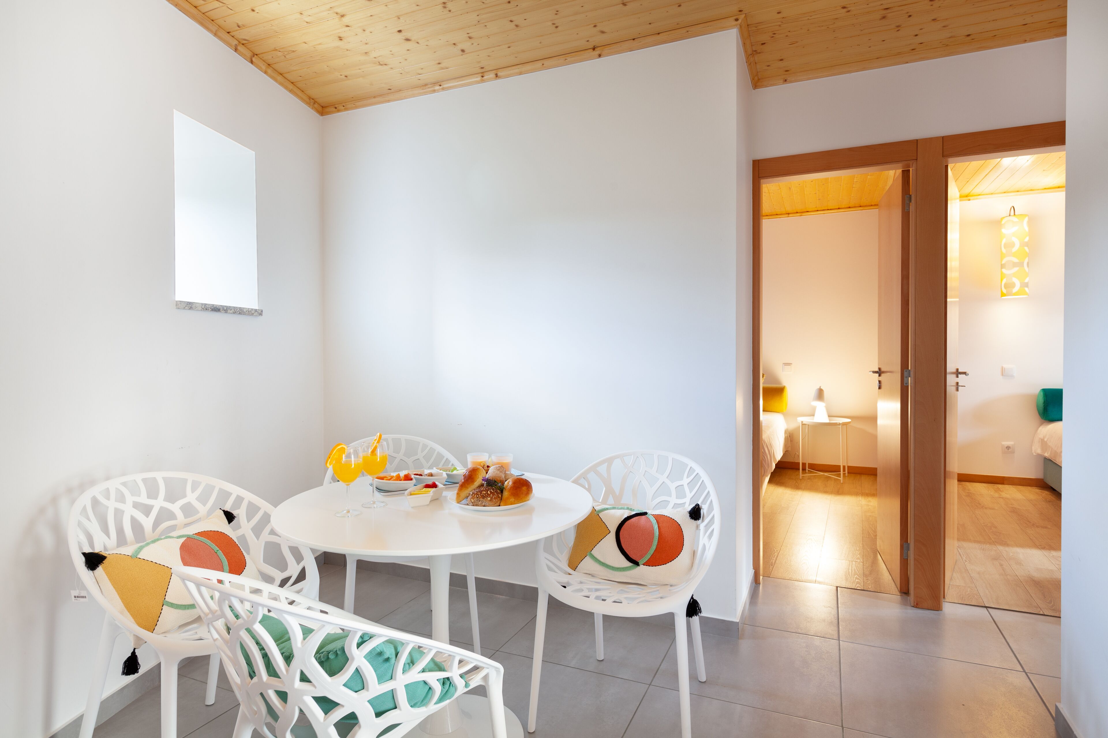 A dining area with a round table and white chairs, a small table with snacks, and a doorway leading to another room.