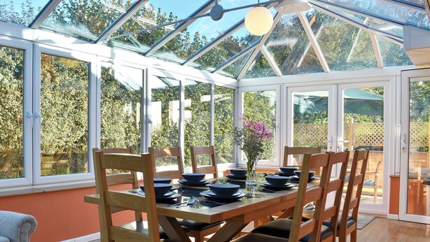 A conservatory with a dining table set for six, surrounded by wooden chairs with black cushions. - 3 bedroom accommodation in Membury, near Axminster (Membury, near Axminster)