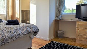 A bedroom with a bed, a desk with a television, a window with curtains, and a view of the outdoors. - 3 bedroom accommodation in Membury, near Axminster (Membury, near Axminster)