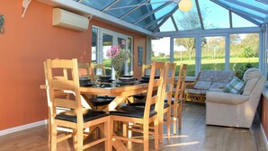A conservatory with a dining table and chairs, a sofa, and a view of a green landscape. - 3 bedroom accommodation in Membury, near Axminster (Membury, near Axminster)