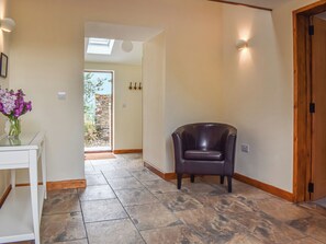 A hallway with a chair, a white table with a vase of flowers, and a door with a wooden frame.