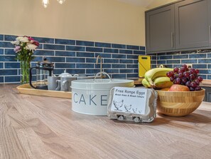 A kitchen counter with a coffee maker, a cake container, a bowl of fruit, and a carton of eggs.