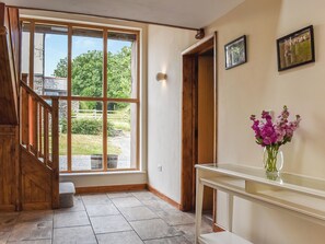 A room with a wooden staircase, a large window with a view of greenery, and a vase with flowers on a console table.