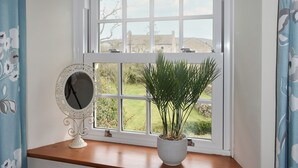 Een kamer met een groot raam, een kamerplant en een decoratieve spiegel op een houten oppervlak.