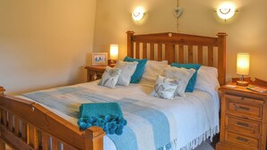 Een slaapkamer met een houten bed, twee bedlampen, een nachtkastje met een ingelijste foto en een houten hoofdbord.