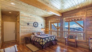 A log cabin bedroom with a bed, a window with a mountain view, and a star decoration on the wall.