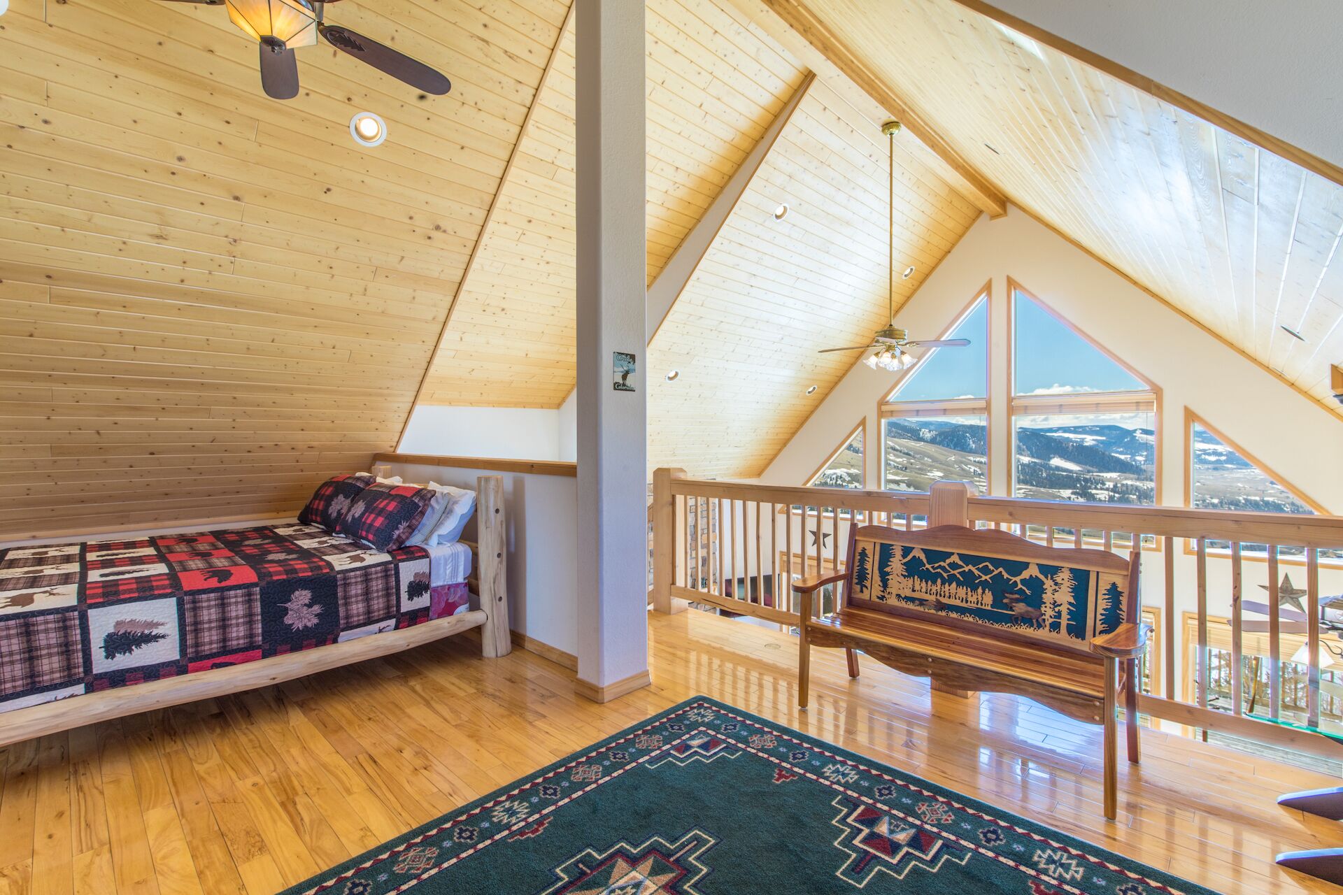 Et soveværelse med skråvægge og loft, træbjælker, en seng med et quiltet dynebetræk, en bænk med et muralmaleri og udsigt til et sneklædt landskab.