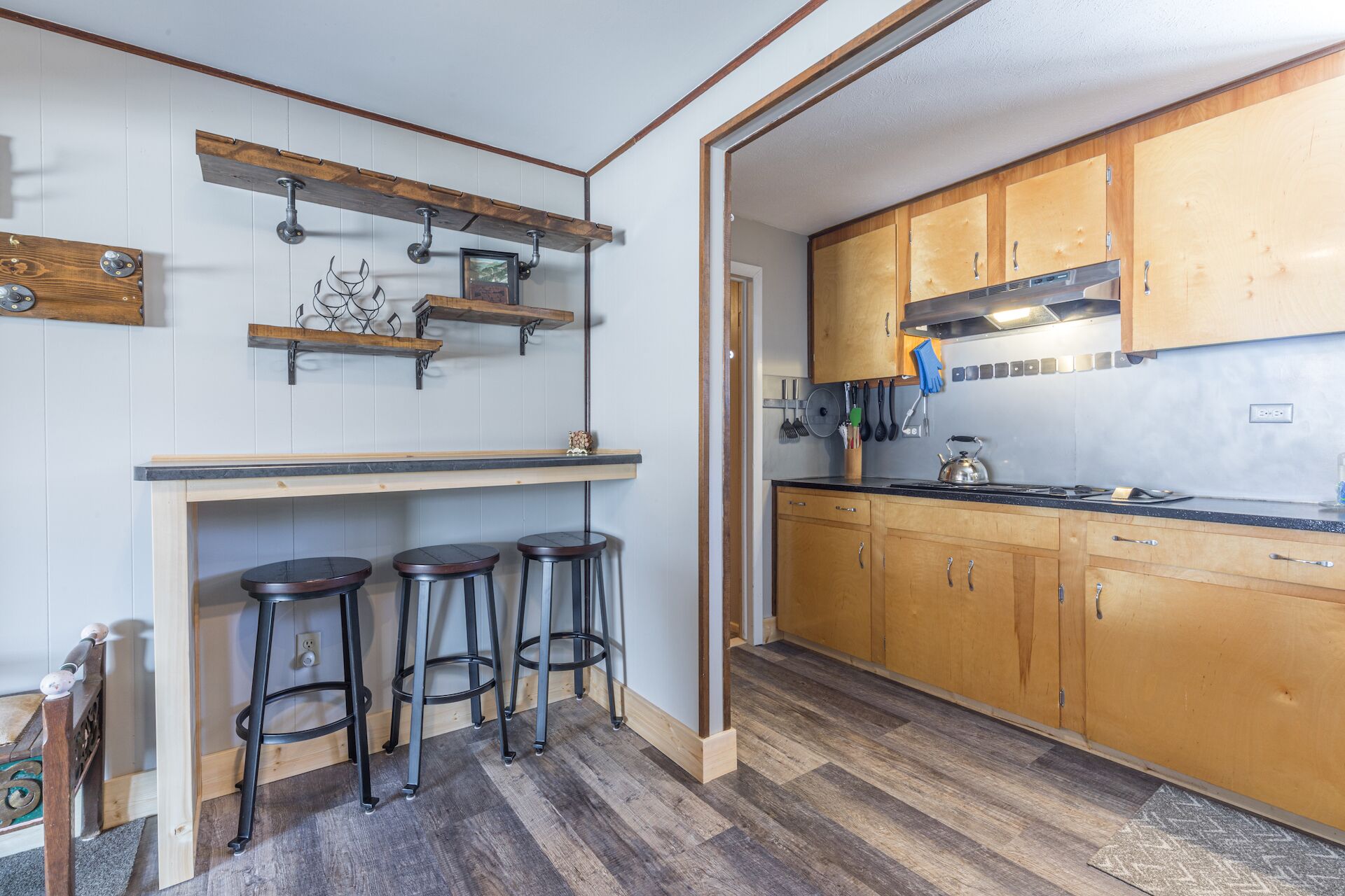 A kitchen with wooden cabinets, a countertop, and three stools.
