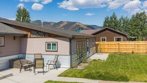 En bostadsfastighet med en uteplats, ett trästaket och en bergssluttning i bakgrunden.