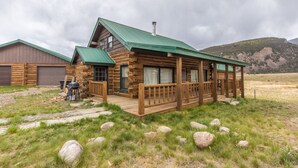 A log cabin with a porch, a garage, and a mountainous backdrop. - Creede Cabin - Dogs Welcome - Amazing Views - Large Deck (Creede)