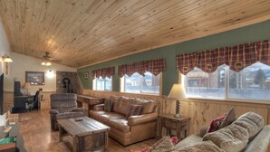 A cozy living room with a wooden ceiling, leather sofas, a wooden coffee table, and plaid curtains.