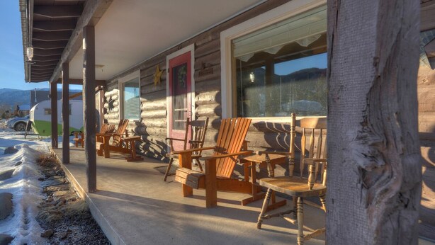 A log cabin with a porch, wooden chairs, and a large window.