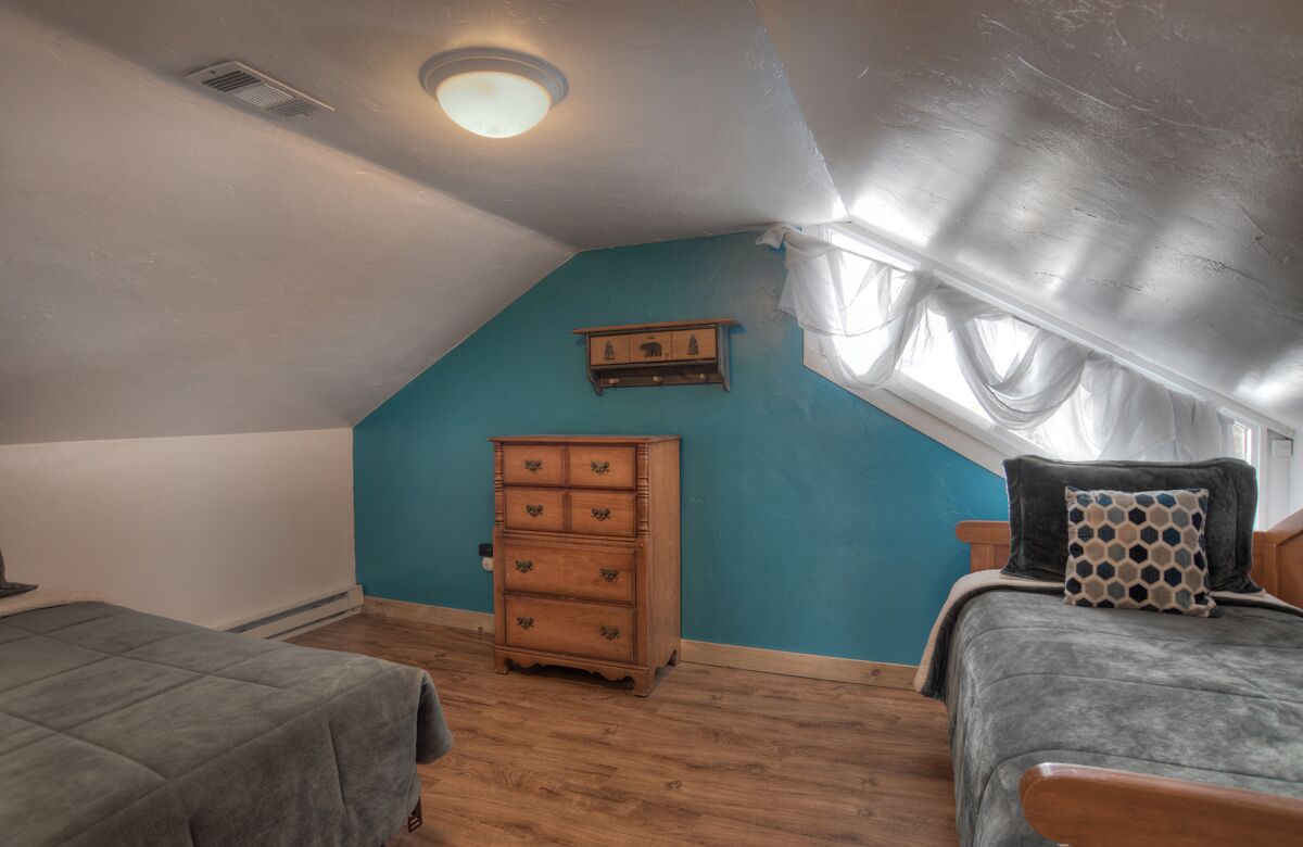 Een slaapkamer met een schuine kap, een houten dressoir, twee bedden en een raam met gordijnen.