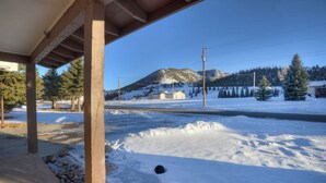 A covered outdoor area with a view of a snow-covered landscape, including a mountain and a building.