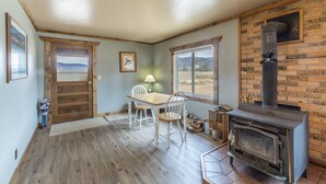Una habitación acogedora con chimenea, suelo de madera, una mesa de comedor con sillas y vistas al exterior.