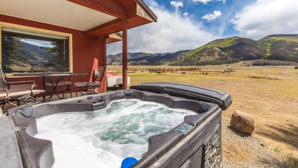 Un jacuzzi con vistas a montañas, un porche cubierto con sillas y una mesa.