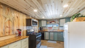Una cocina con paredes de madera, estufa a gas, microondas, refrigerador y ventana con vistas.