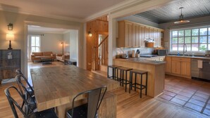 A spacious kitchen with wooden cabinets, a large island with stools, and a dining area with a wooden table and chairs. - Historic Home | Pet Friendly | Walkable to Downtown (Creede)