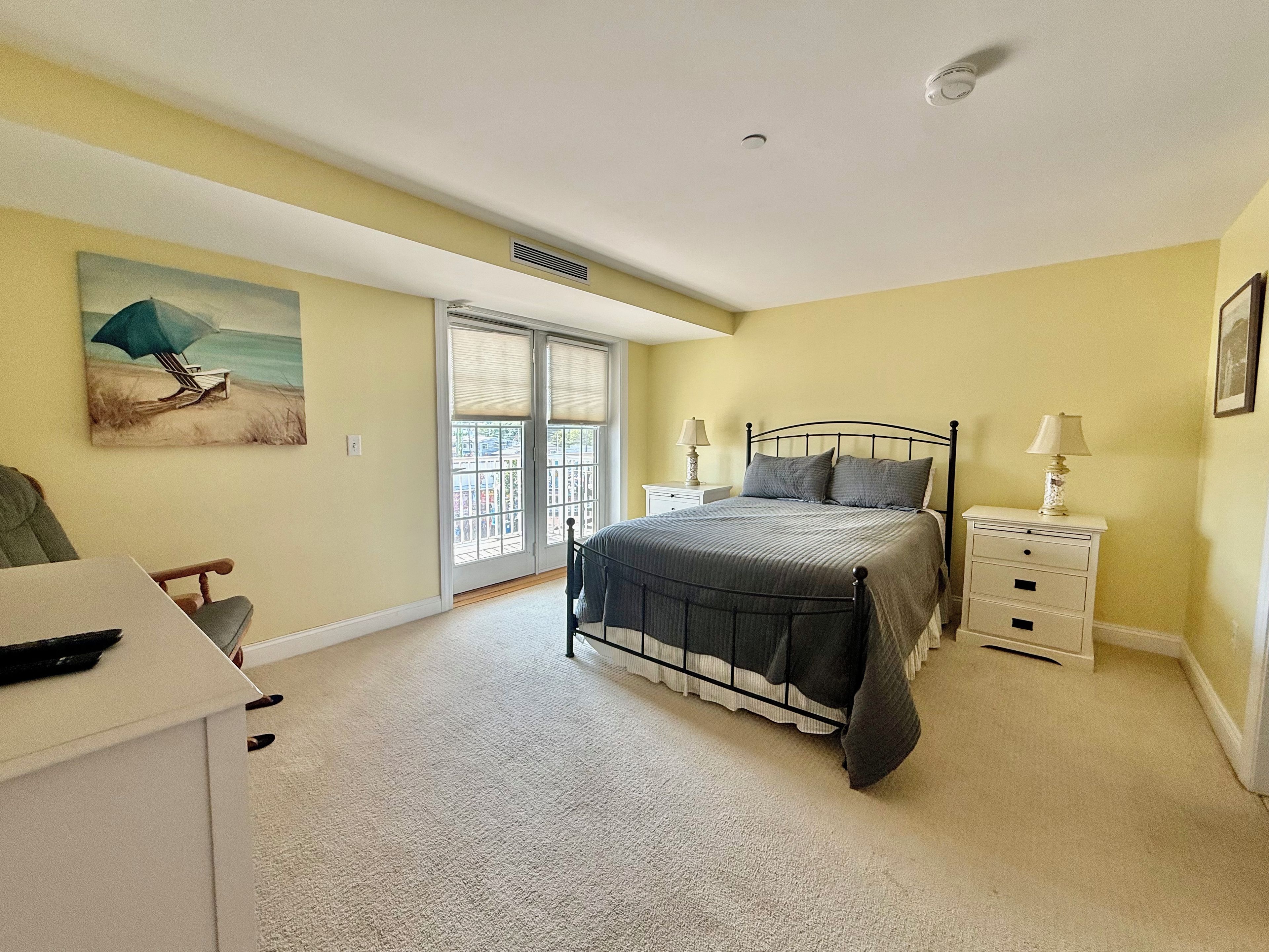 Un dormitorio con cama, mesitas de noche, una silla y un cuadro en la pared.