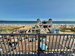 Un muelle en la playa con un letrero que dice 'The Pier' y vista de la playa, gente y sombrillas.