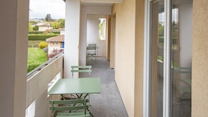 A balcony with a table and chairs, a glass door, and a view of the neighborhood.