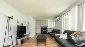 A modern living room with a fireplace, a black leather sofa, a TV on a stand, and a wooden floor. - 🏖 Sandy Hook: 2 Queens, Pet Friendly, One Min to Beach, Ice Fishing and Snaks (Sandy Hook)