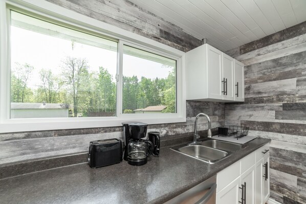 A kitchen with a large window, a sink, and a coffee maker.