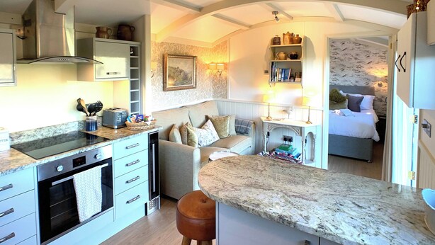Une cuisine compacte dotée d’une cuisinière intégrée, un coin repas avec une table et des chaises, et une chambre à coucher avec un lit et une table de chevet.