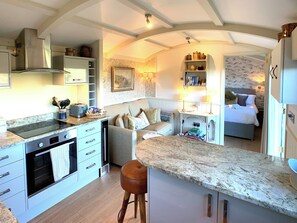 Une cuisine compacte dotée d’une cuisinière intégrée, un coin repas avec une table et des chaises, et une chambre à coucher avec un lit et une table de chevet.